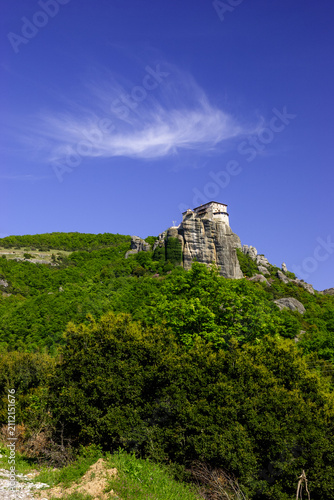 The Monastery of Great Meteoron perched atop a rock formation in Meteora, Greece, under a clear blue sky with wispy clouds.