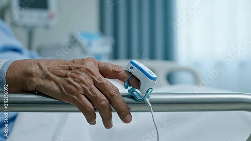 Close-Up View Of A Hospital Patient's Hand Resting On A Bed Rail With A Pulse Oximeter Monitoring Health