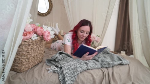 Young woman with red hair lying in cozy canopy bed reading a book, peaceful morning routine at home