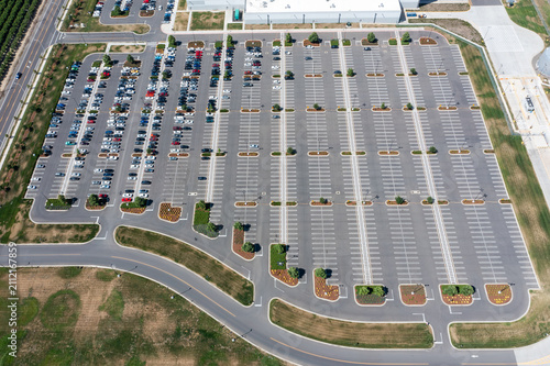 Aerial drone photo of a large commercial parking lot with parked cars beside an industrial warehouse and distribution facility in Woodburn, Oregon, USA on a clear summer day