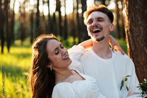 Konstfotografi Joyful couple laughing together in a sunlit forest during a wedding photoshoot