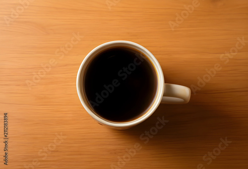 Overhead view of a white ceramic coffee mug filled with black coffee on a light wooden table surface