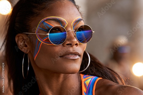 Stylish woman with colorful face paint and sunglasses outdoors