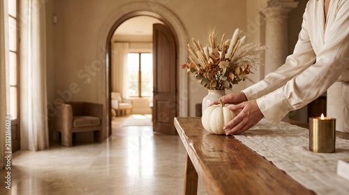 Person decorating rustic table with white pumpkin and dried botanical arrangement for autumn