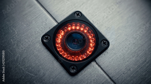 Security camera equipped with red glowing infrared night vision lights is mounted securely on a metallic industrial panel surface.