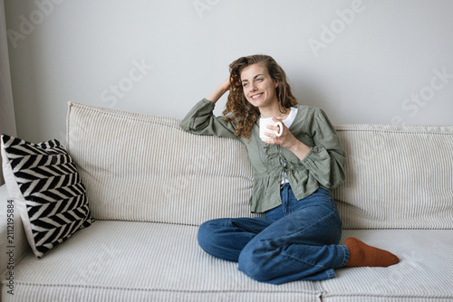 Young woman having a relaxing coffee or tea break on the sofa at home