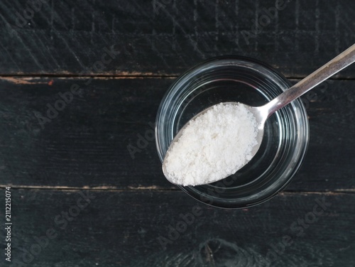 Photography Salt water solution in a glass with a spoon of sea salt on dark wooden background