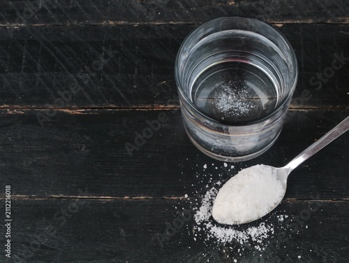 Canvas Print Salt water solution in a glass with a spoon of sea salt on dark wooden background