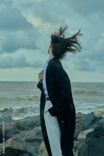 Obraz na płótnie Windy coastal scene with a woman in a blazer and white pants facing the sea, hai