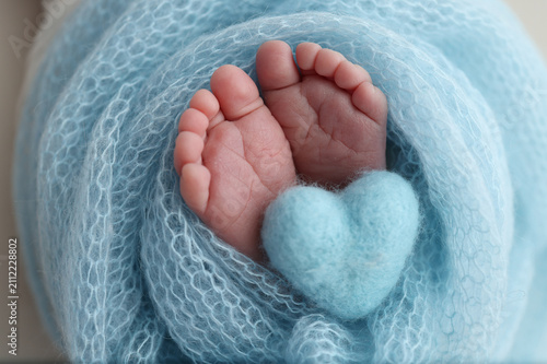 Canvas Print Newborn baby feet with a heart shape against blue knitted fabric closeness prote