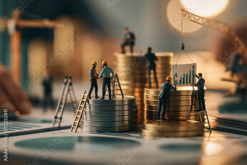 Miniature business people build a financial structure using stacks of golden coins as platforms reflecting strategic growth economic planning and collaborative corporate project management