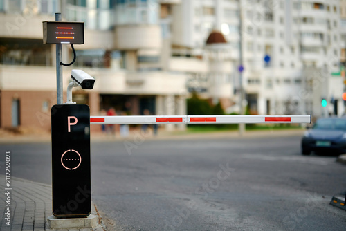 Parking access control system with surveillance camera. security boom barrier at residential building entrance. Automatic parking barrier gate with security surveillance camera and illuminated P sign