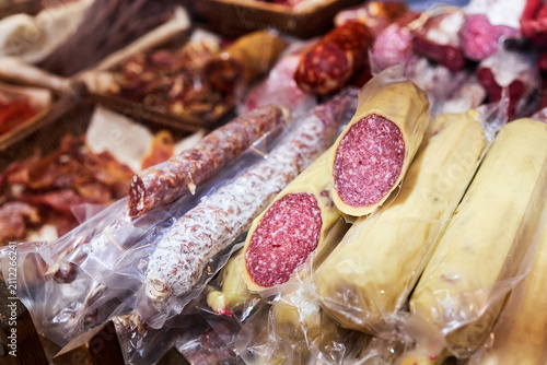 Traditional cured sausages and deli meats displayed at farmers market. Various types of smoked and dried meat products for sale in baskets and on counter.