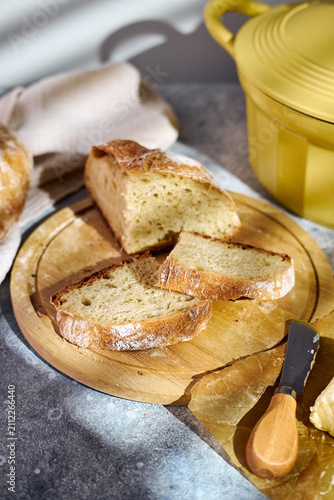 Close-up of a freshly baked artisan loaf cut in half, revealing porous crumb structure. Stacked on a wooden board with butter and linen cloth nearby.