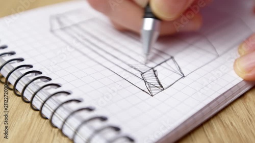 Close up shot of hand drawing geometric sketch with pen on spiral notepad. Person creating technical illustration on paper page.