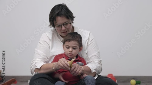 Mother teaching her toddler son how to peel a banana