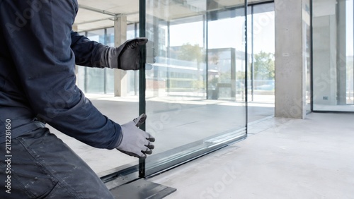Construction worker installing glass partition wall in commercial office space with construction partition installing renovation commercial