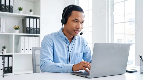 Indonesian business man speaking having virtual meeting on laptop. Wearing headset talking consulting on video call at home office call center.
