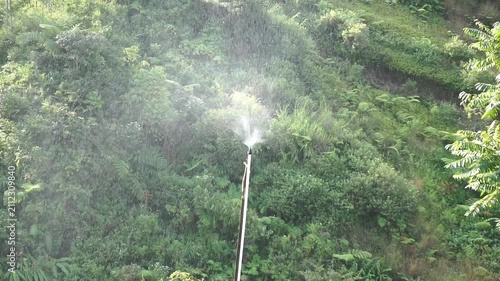 An automatic water sprinkler spraying water on a fertile hillside agricultural farm land area.