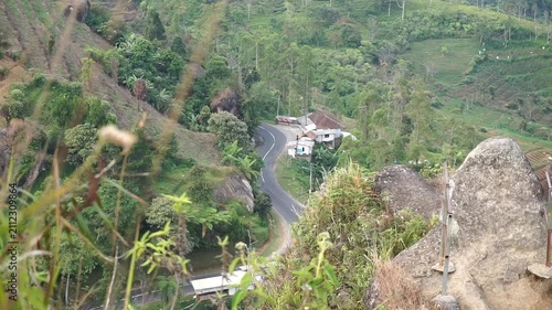 High angle view of a winding asphalt road on a mountain slope surrounded by trees and rocky cliffs.