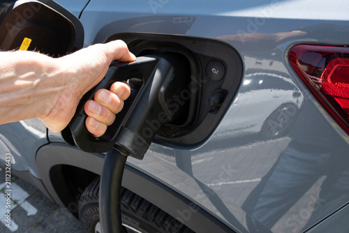 A man's hand is plugging a charging cable into an electric car