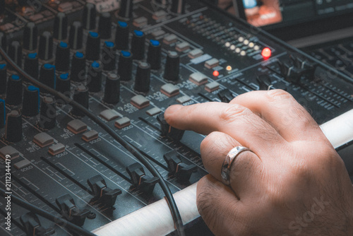 Close-up of a hand adjusting a knob on an audio mixing console in a studio, featuring a vintage warm cinematic color grading. Professional music production concept.