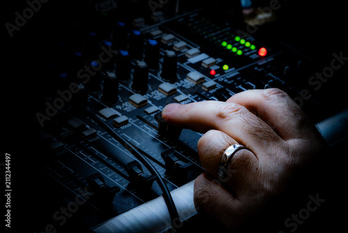 Close-up of a hand adjusting a knob on an audio mixing console in a dark studio. Professional sound engineer working on a music mixer board under dramatic lighting.