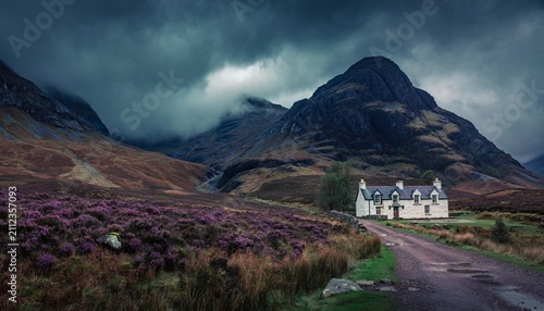 Mountains stand behind a house on a road with purple flowers in a valley during cloudy weather in Scotland
