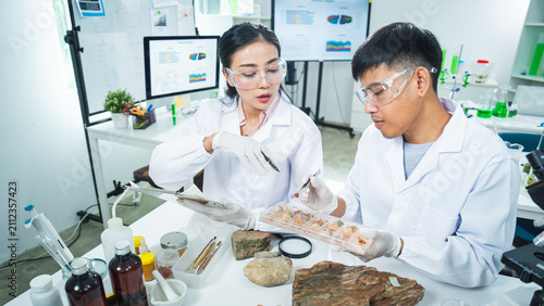 Scientist laboratory research fossil rock microscope specimen geology study with Asian adult researcher wearing lab coat and protective eyewear examining natural sample