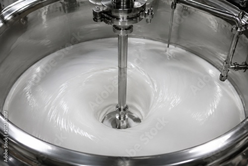 White slurry rotating inside a polished industrial mixing tank, creating smooth ripples on the surface.