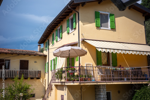 Bright yellow house with green shutters and a balcony in a rural area during the day