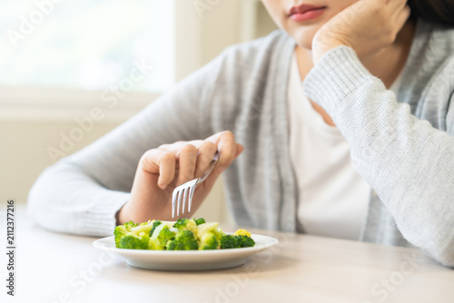 Obraz na płótnie Diet in bored concept, Ketogenic, Low carb, Intermittent Fasting young woman dieting holding fork at broccoli on salad plate tired with eat fresh vegetables