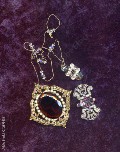 Vintage small jewelry a bit kitch, brooches and neklace on purple velvet background