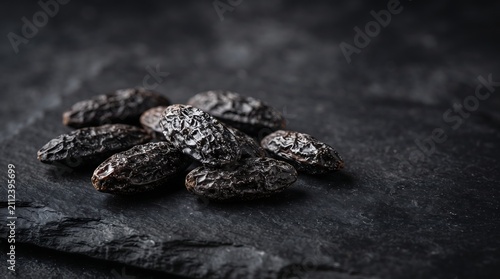 Close up of tonka beans piled on dark slate background with dramatic lighting.