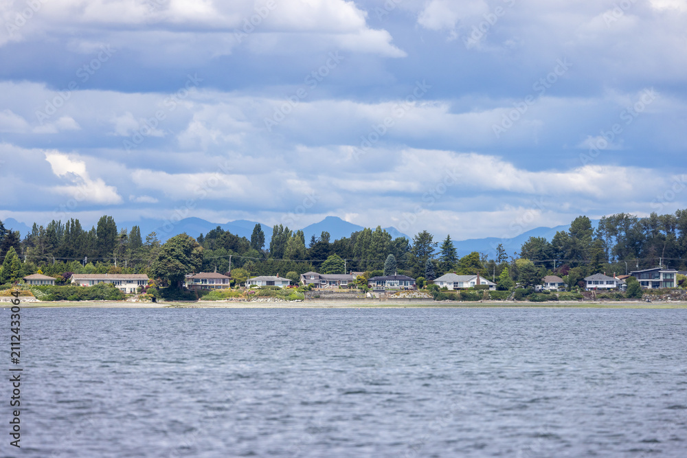 Fototapeta premium Waterfront Homes Along Sidney Shoreline With Mountains And Cloudy Sky on Vancouver Island BC