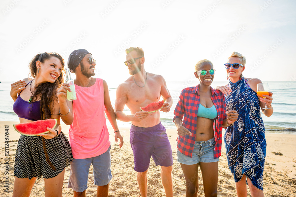 Obraz premium Group of friends enjoying watermelon and drinks on a sunny beach.