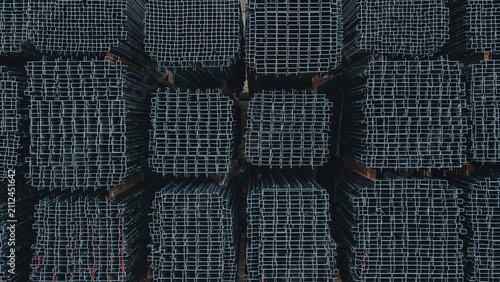 Stacked metal pipes or beams arranged in a grid pattern, viewed from above, with a dark background. Infrastructure and construction materials. Storage and organization of metal components.
