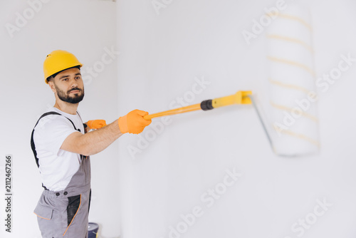 Bild auf Leinwand Professional painter working indoors, applying white paint with a roller on a wa