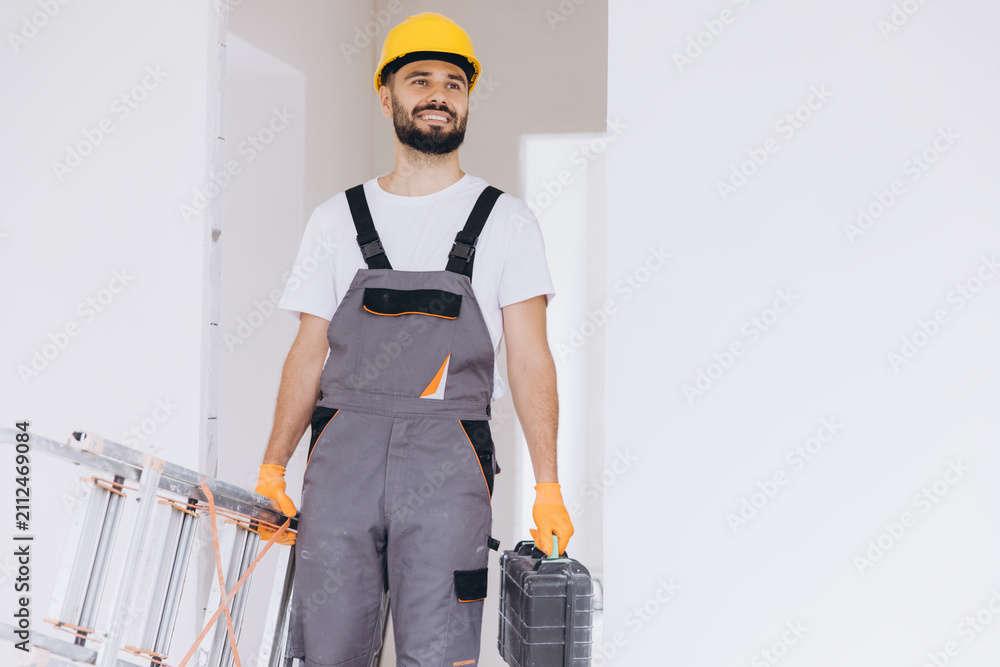 Obraz premium Smiling construction worker carrying a ladder and toolbox, ready for home renovation or repair work