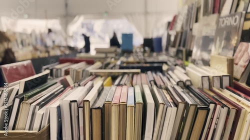 Rows of vintage hardcover books filling cardboard boxes at a bustling flea market stall, with many people browsing through the extensive collection of second-hand literature in the background