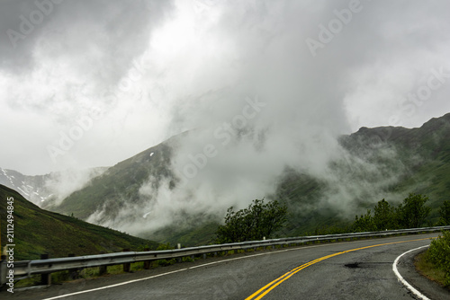 Fotografía Winding mountain road with guardrail heading through low clouds and thick fog in