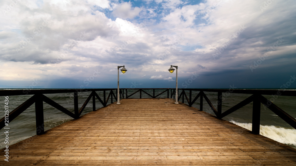 Fototapeta premium Wooden pier with lamps leading to the sea under a dramatic cloudy sky