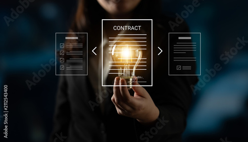 Obraz na płótnie A businesswoman showcases a glowing light bulb representing innovation and creativity while engaging with digital contract documents in a modern office setting
