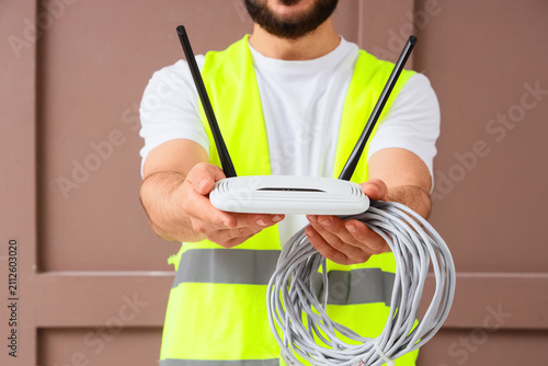 Fotografie Technician in safety vest holding a white wireless router and coiled ethernet ca