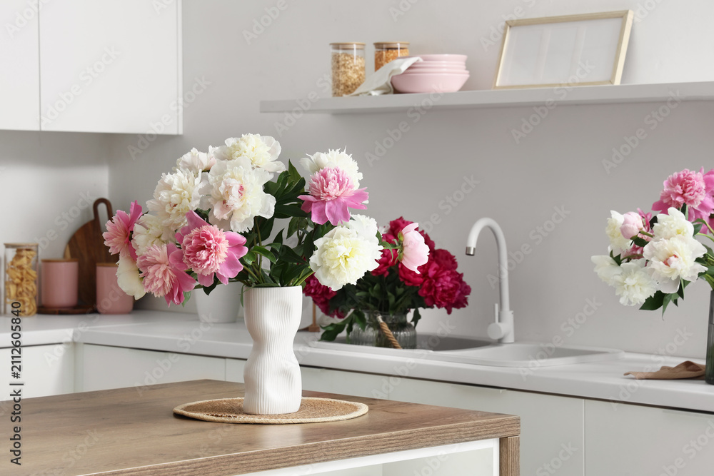 Obraz premium Pink and white peony flowers in a modern white vase on a wooden kitchen island with a clean minimalist background