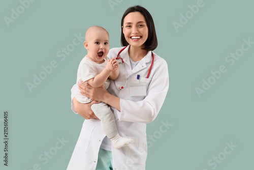Young female pediatrician with happy little baby on green background