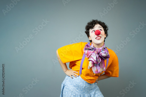 Young woman dressed as a clown, looking upwards. Horizontal studio portrait with copy space, ideal for circus art, children's party, and fun entertainment.
