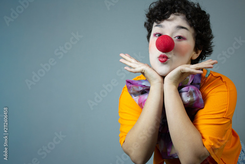 Funny young woman dressed as a clown, blowing a kiss. Horizontal studio portrait with copy space, ideal for circus art, children's party, and fun entertainment.