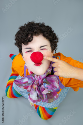 Young lady dressed as a clown, pointing at her nose. Vertical studio portrait with copy space, ideal for circus art, funny character, and entertainment.