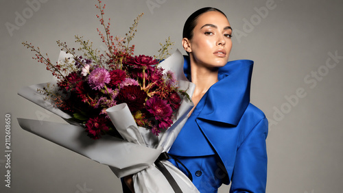 Woman in a blue tailored suit holding a large floral bouquet. Ideal for fashion editorials, florist campaigns, luxury branding, beauty ads and posters.
